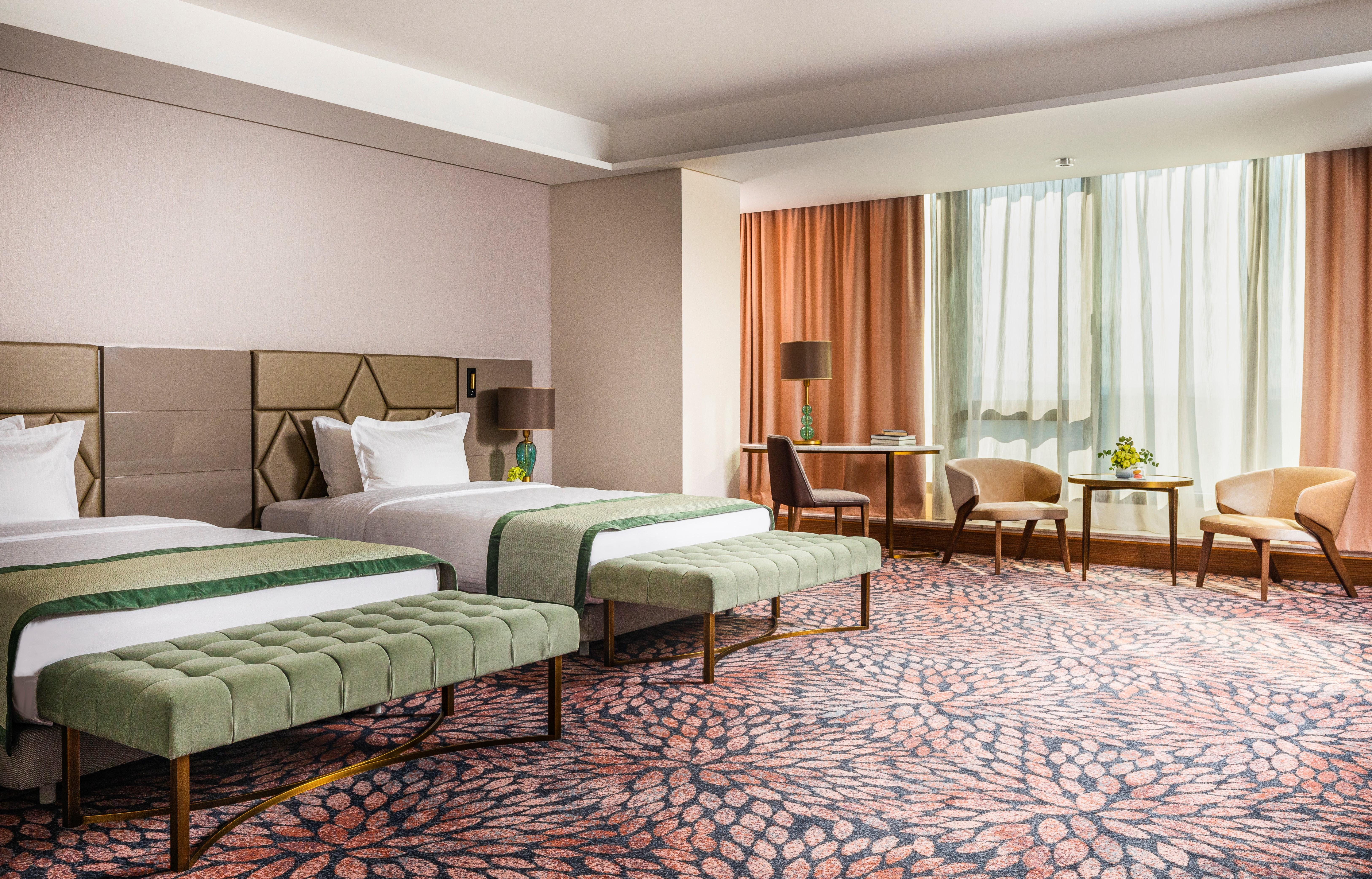Grand Hotel Millennium 소피아 외부 사진 The image shows a well-decorated hotel room featuring two beds with green striped bedspreads. There is a plush green bench at the foot of each bed. The room has large windows with sheer curtains allowing natural light to enter. There is a cozy seatin