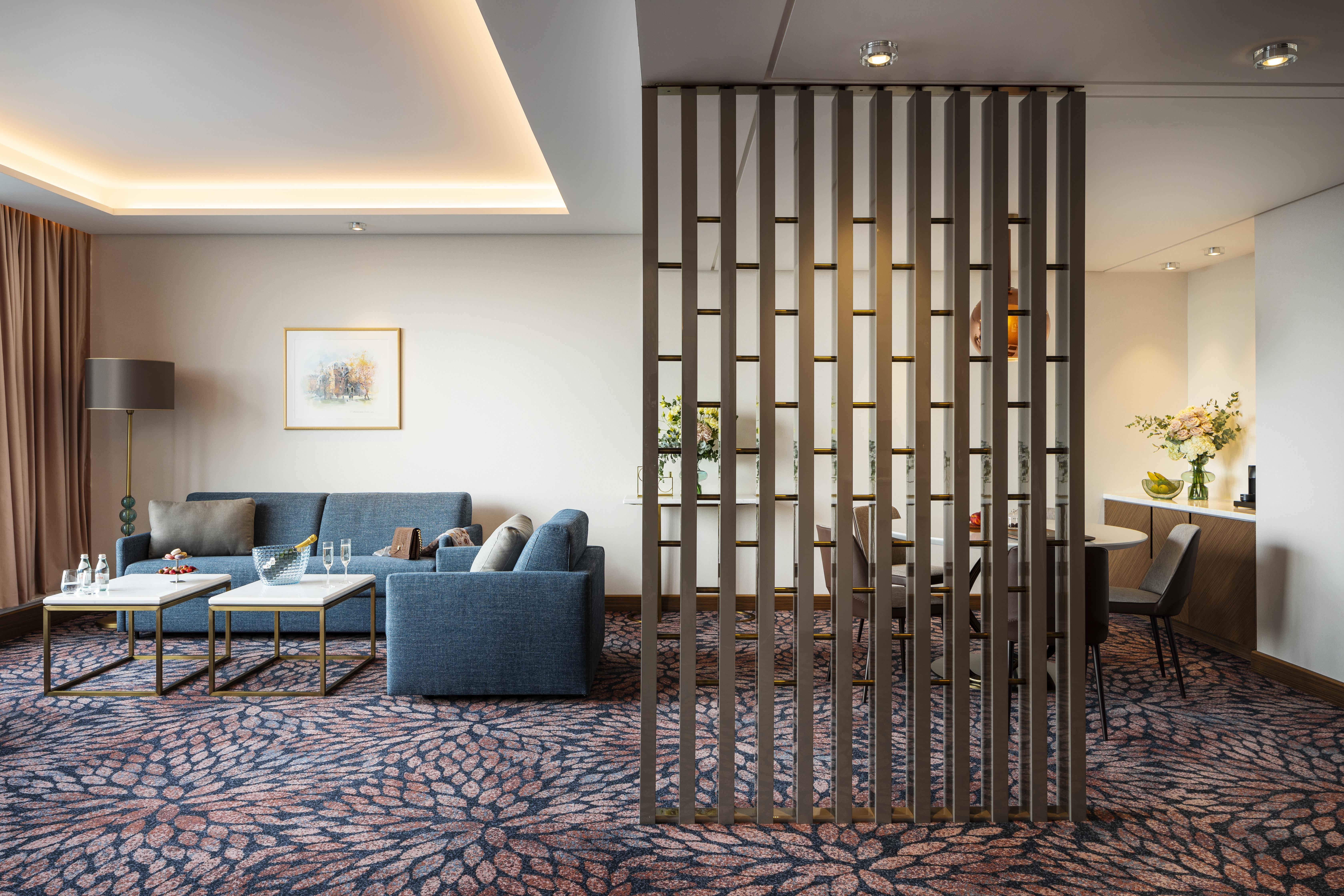 Grand Hotel Millennium 소피아 외부 사진 The photo shows a modern living space with a comfortable seating area featuring a blue couch and two coffee tables. There is a decorative partition made of vertical wooden slats, which separates this sitting area from a dining space. The dining area 