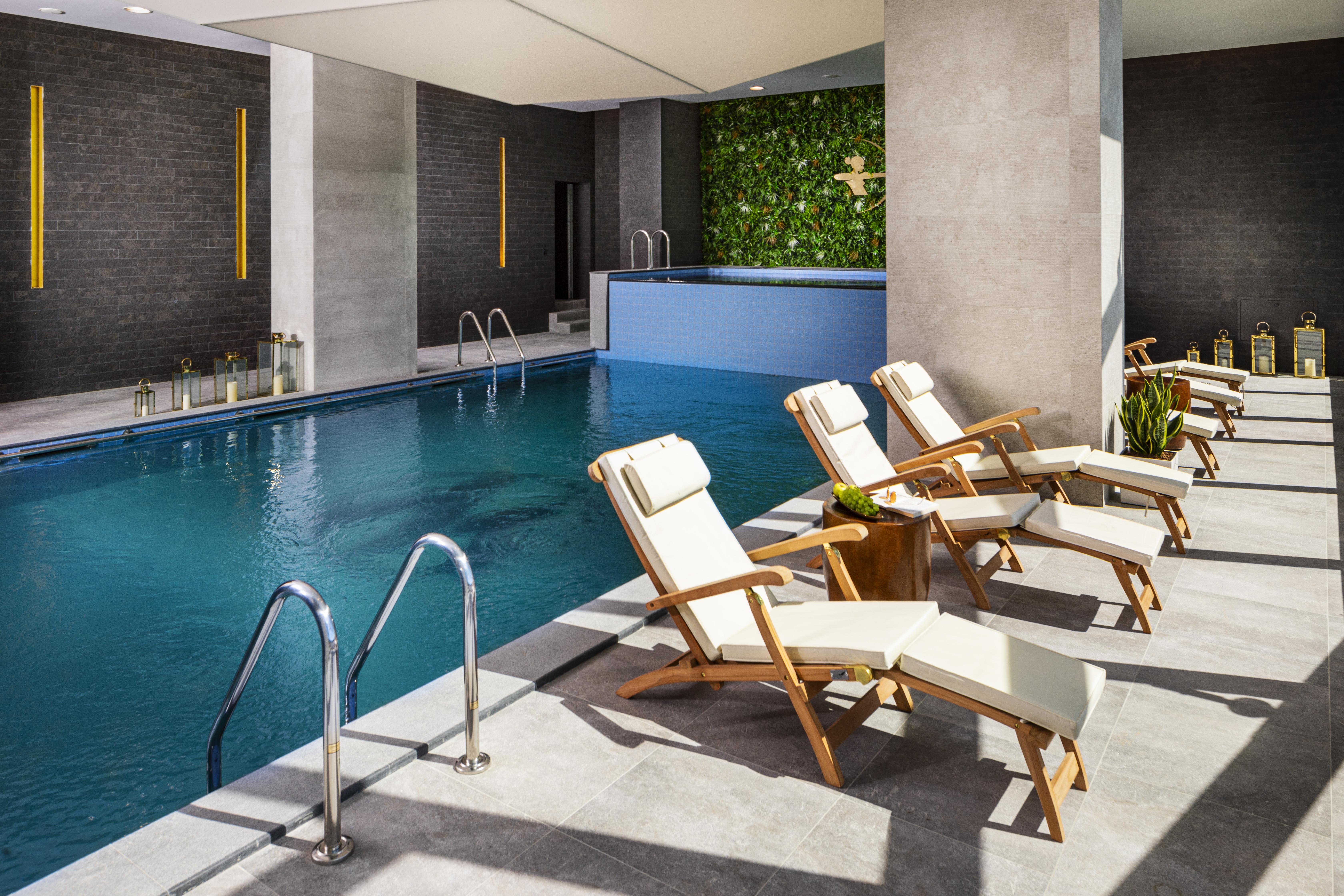 Grand Hotel Millennium 소피아 외부 사진 The photo shows a serene indoor swimming pool area. The pool is clear and inviting, with a blue water surface reflecting light. Along one side of the pool, there are several light-colored lounge chairs with white cushions, positioned for relaxation. 